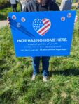 A blue poster with a heart colored like the US Flag. Motto on the poster says Hate has no Home Here.