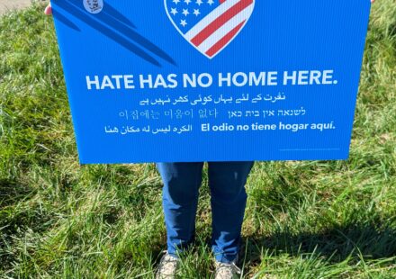 A blue poster with a heart colored like the US Flag. Motto on the poster says Hate has no Home Here.